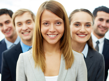 Eine Gruppe von jungen Geschäftsleuten steht versetzt hintereinander und lächelt in die Kamera.